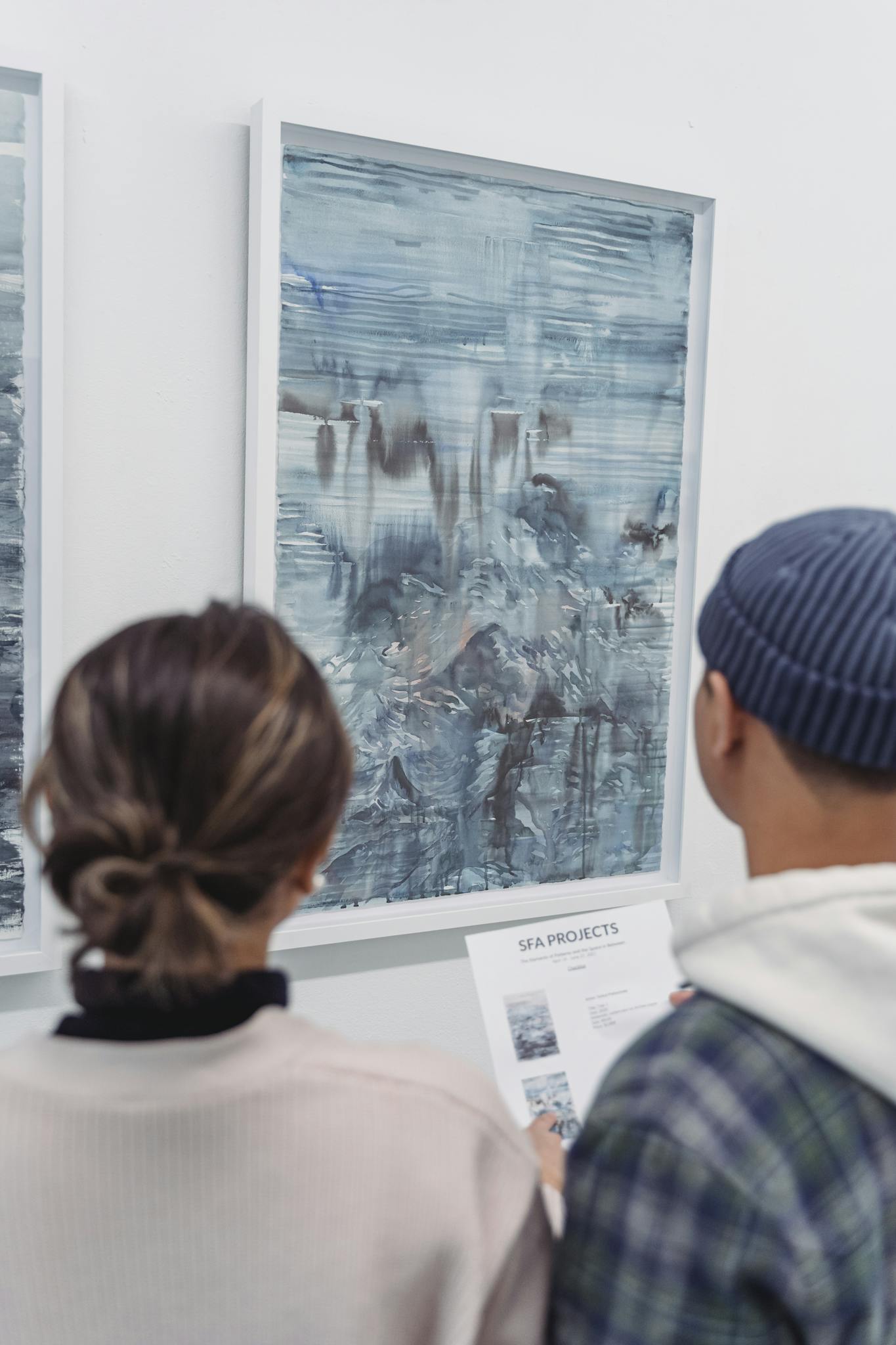 Two people view abstract art in a modern gallery, focusing on interpretations.
